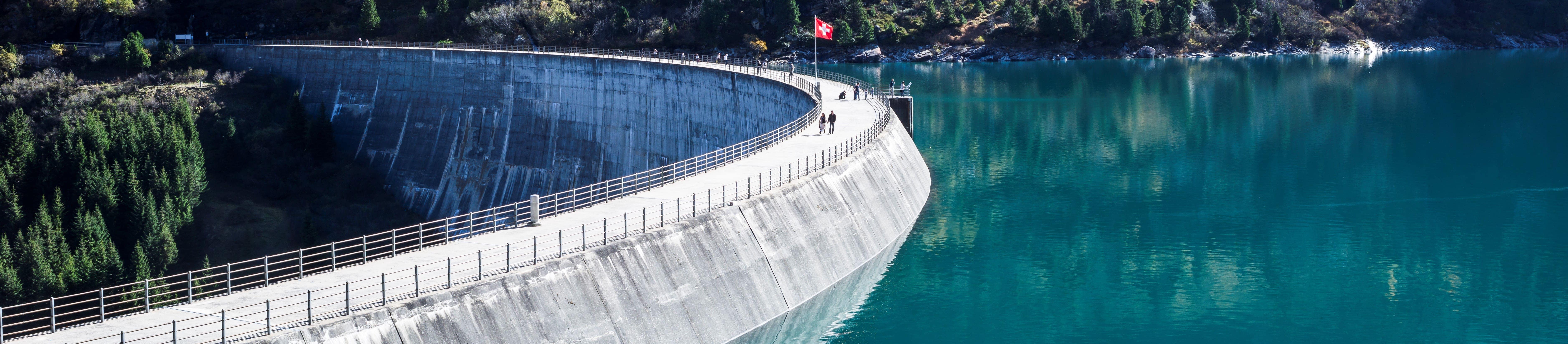 Staudamm mit Schweizerflagge und Menschen drauf