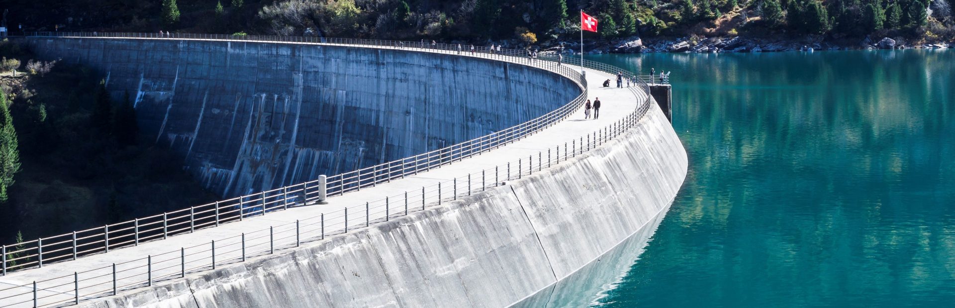 Staudamm mit Schweizerflagge und Menschen drauf